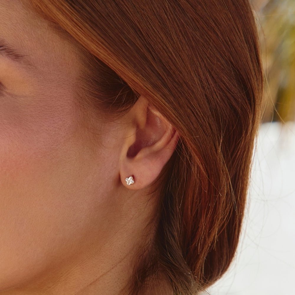 Golden Crystal Clover Stud Earrings, worn in an ear, close-up of a small silver flower stud
