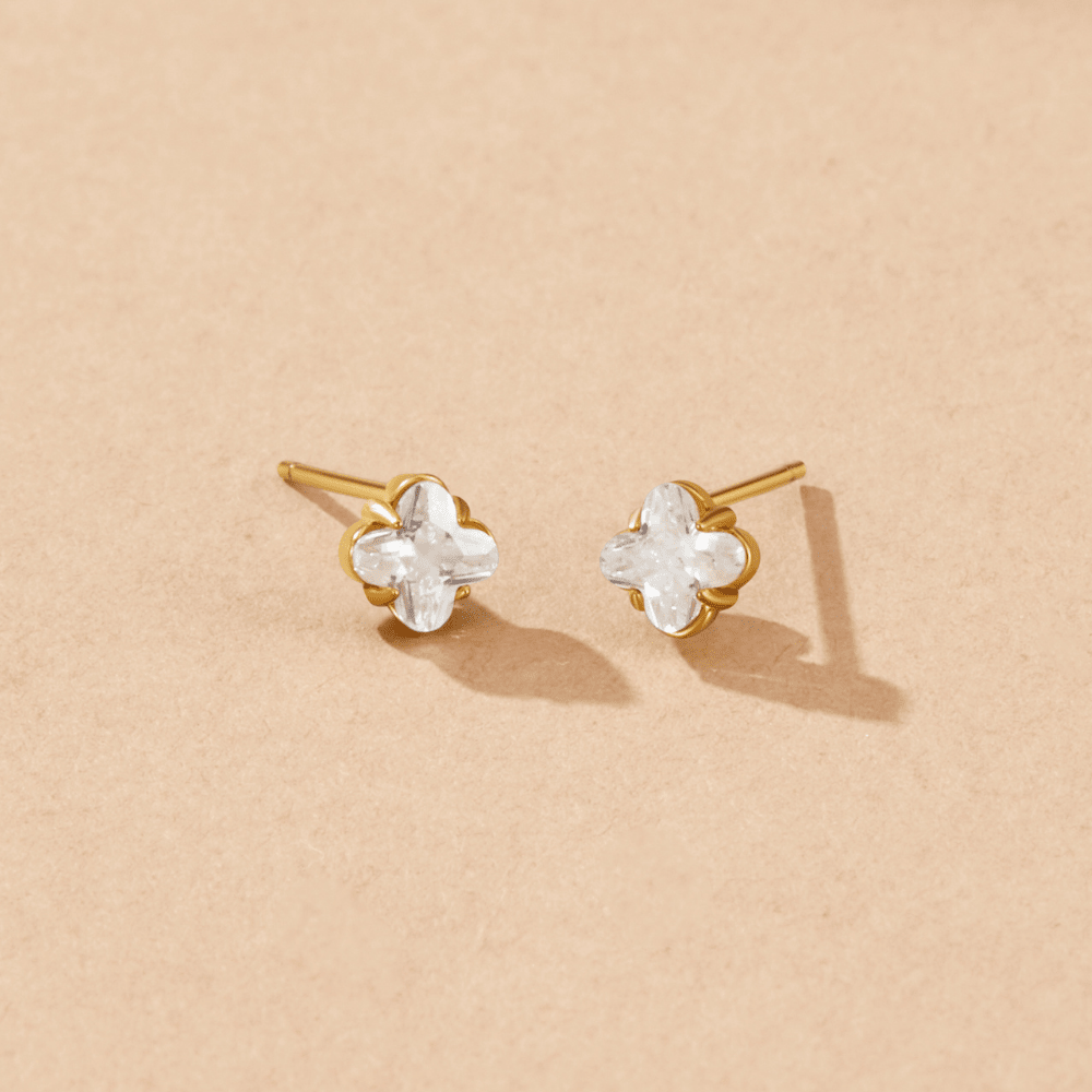 Golden Crystal Clover Stud Earrings, a pair of clover-shaped clear stones in gold settings on beige